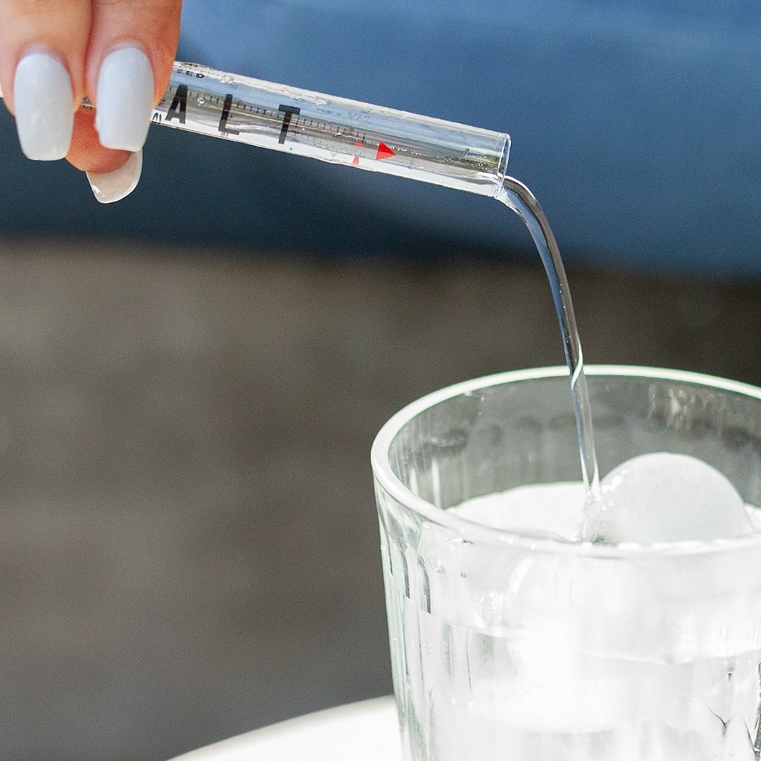 Close-up of a hand pouring liquid from a glass dropper into an iced glass of water